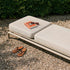 Beige Kirra Sunbed van sackit op een grindterras met zachte kussens een boek en sandalen in de zon