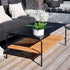 Zwart buiten salontafel van gepoedercoat aluminium met teakhouten onderblad naast een donkere loungesofa op een houten terras met groene plant