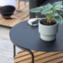 Rond zwart buitenbijzettafeltje met plant in pot en teakhouten plank onderaan op een modern terras ontworpen voor nordisch weer door sackit