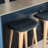 Twee barkrukken van eikenhout met zwarte leren zittingen aan een kookeiland, ontworpen in Denemarken door sackit voor een modern interieur