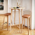 Twee hoge barkrukken van eikenhout met cognackleurige leren zittingen aan een ronde bartafel in een licht Scandinavisch interieur van sackit