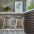 Twee Nordic barkrukken van massief eikenhout met zwarte leren zittingen en zichtbare stiksels in een modern interieur met planten en bakstenen muur van sackit Nederland