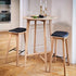 Twee barkrukken van massief eikenhout met zwarte leren zittingen naast een hoge ronde tafel in een stijlvol Scandinavisch interieur van sackit