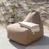Beige outdoor loungestoel van sackit in de duinen met een zachte plaid over de rugleuning en een metalen drankhouder naast de stoel