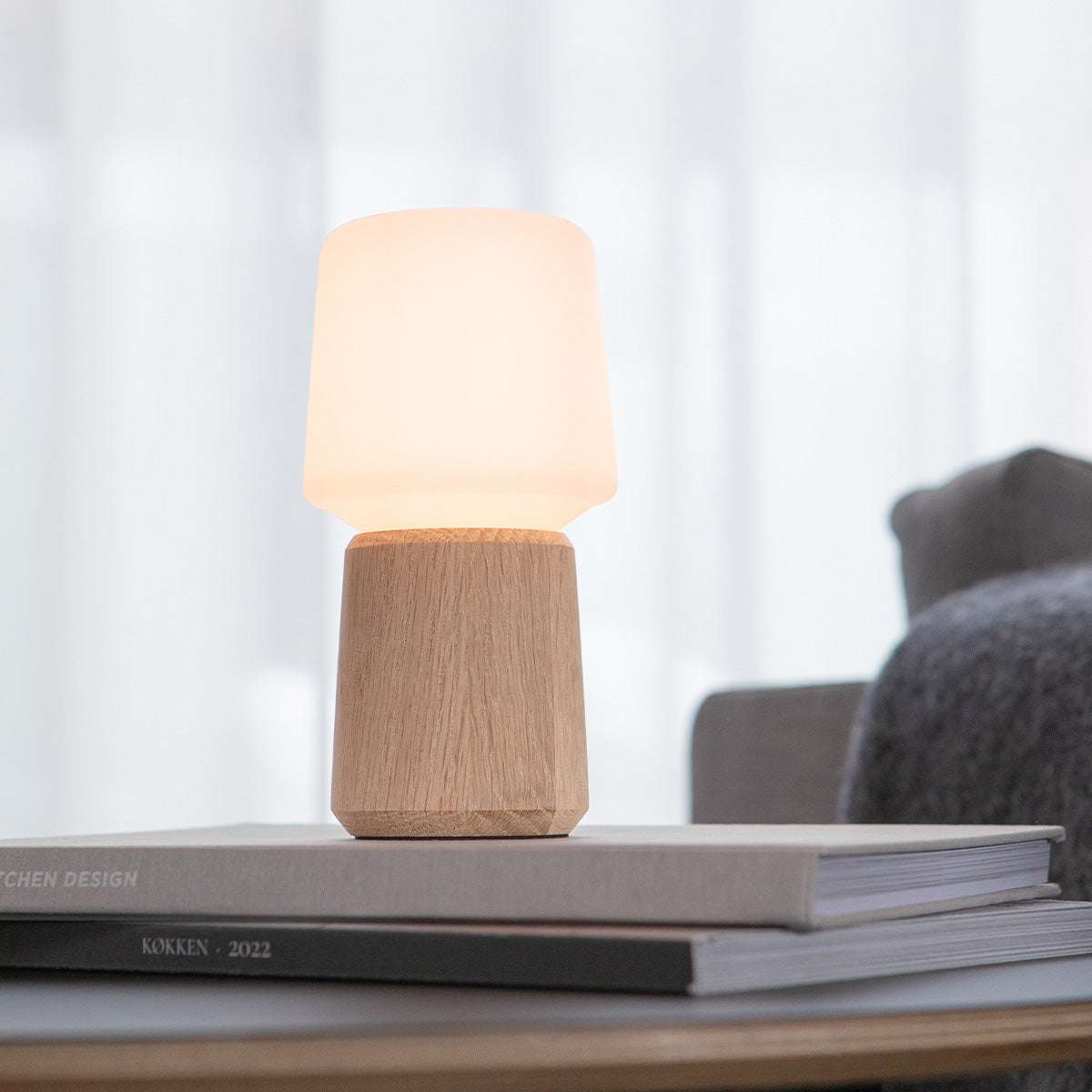 Houten lampvoet van sackit met warme lampenkap op een stapel boeken in een rustig Scandinavisch interieur、】【