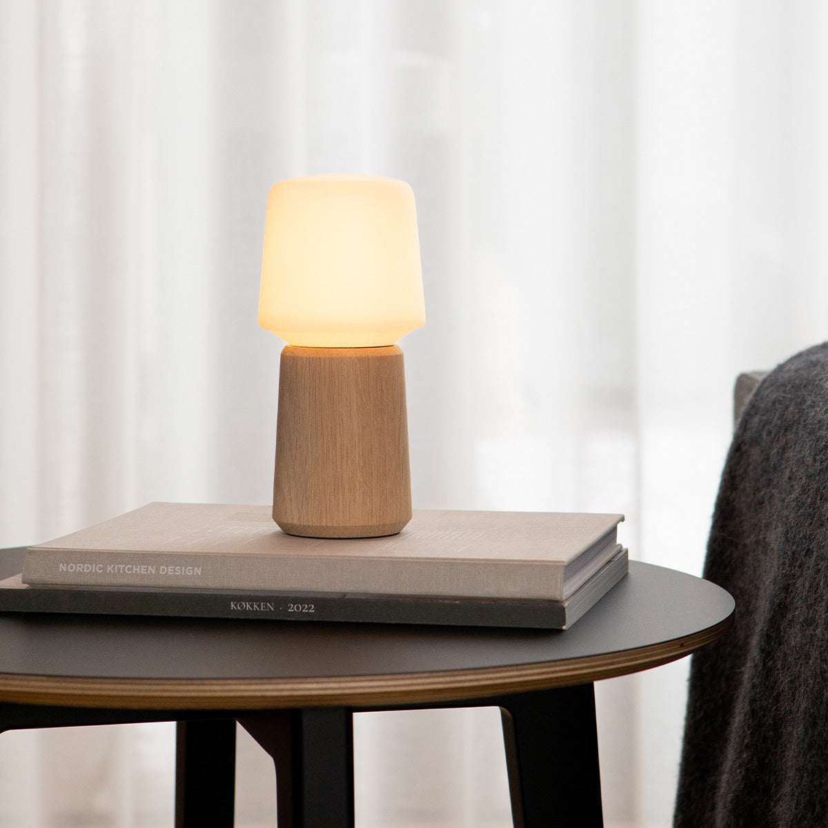 Houten lampvoet met zachte warme verlichting op een stapel boeken op een ronde tafel in een Scandinavisch interieur van sackit
