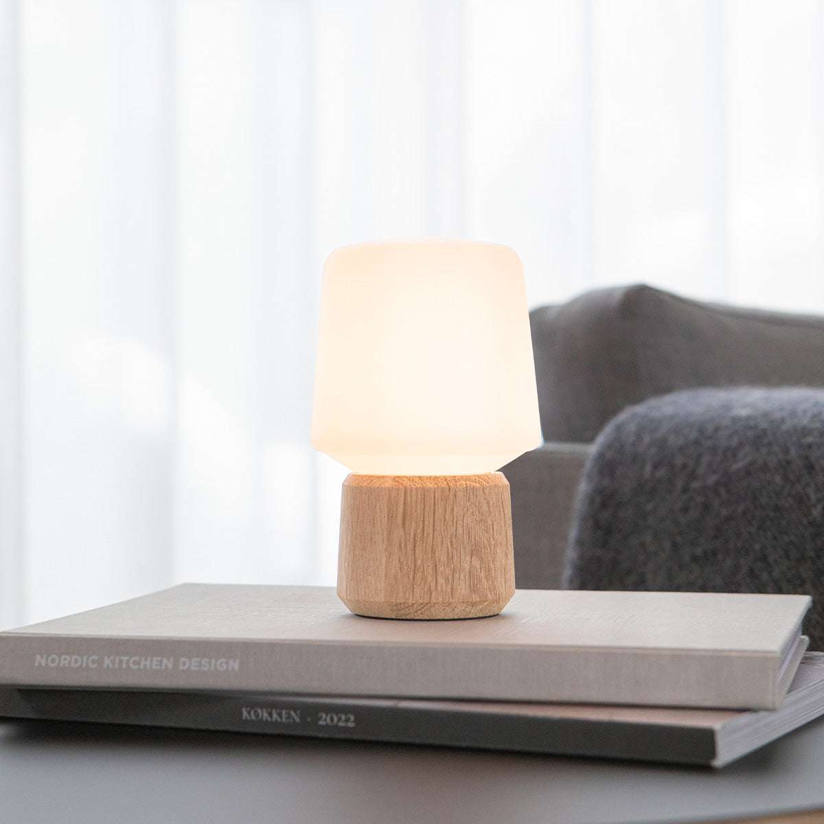 sackit draadloze tafellamp met warme verlichting en houten voet op boeken in een stijlvol interieur van premium Deens meubeldesign