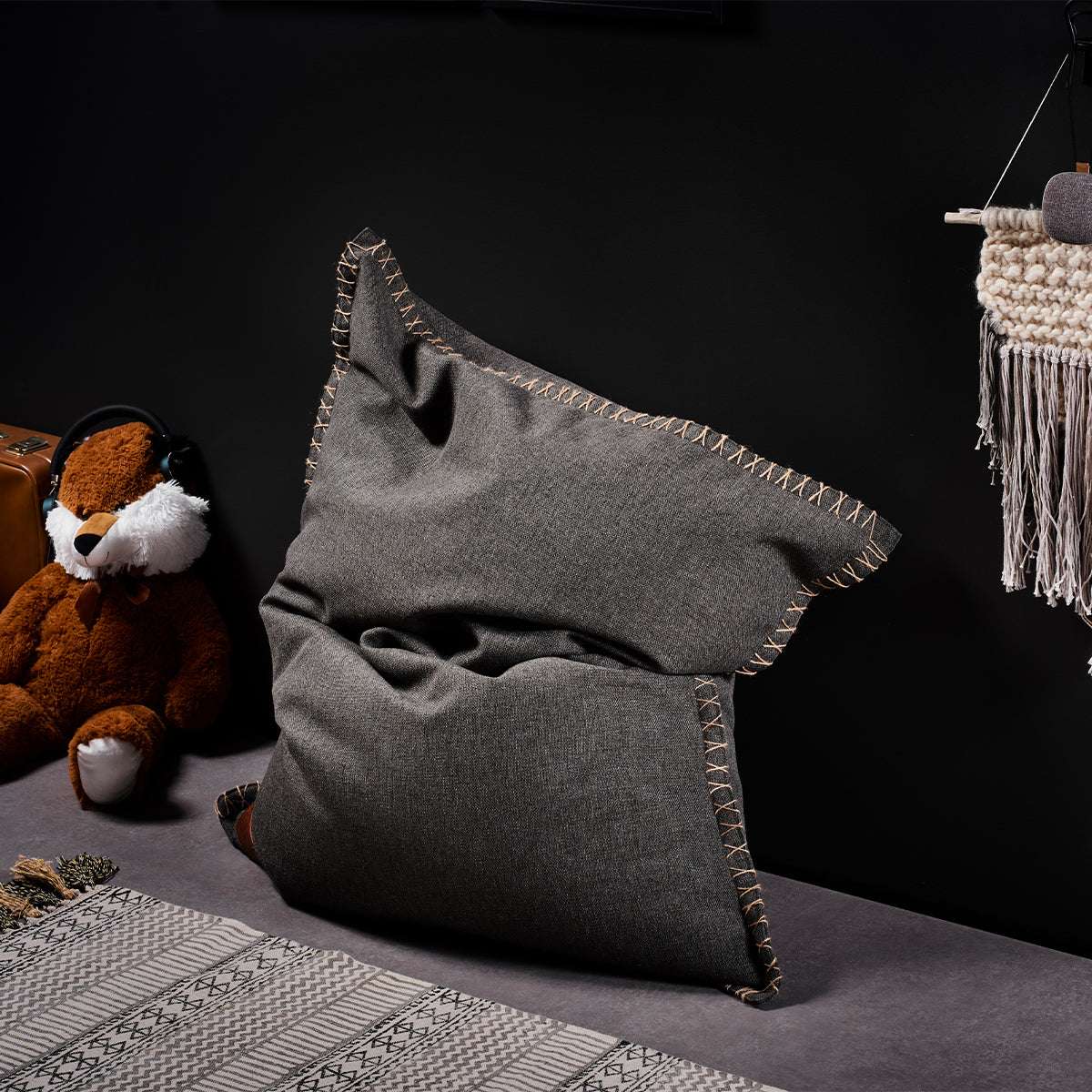 Grijze kinderzitzak van sackit in een modern interieur met een knuffelbeer en plaid. Comfortabele stoel voor kinderen binnen en buiten
