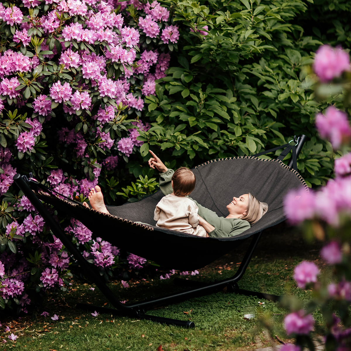 Zwarte buitenhangmat van sackit met moeder en kind in een bloeiende tuin en comfortabele ligruimte voor ontspanning buiten bij zonnig weer