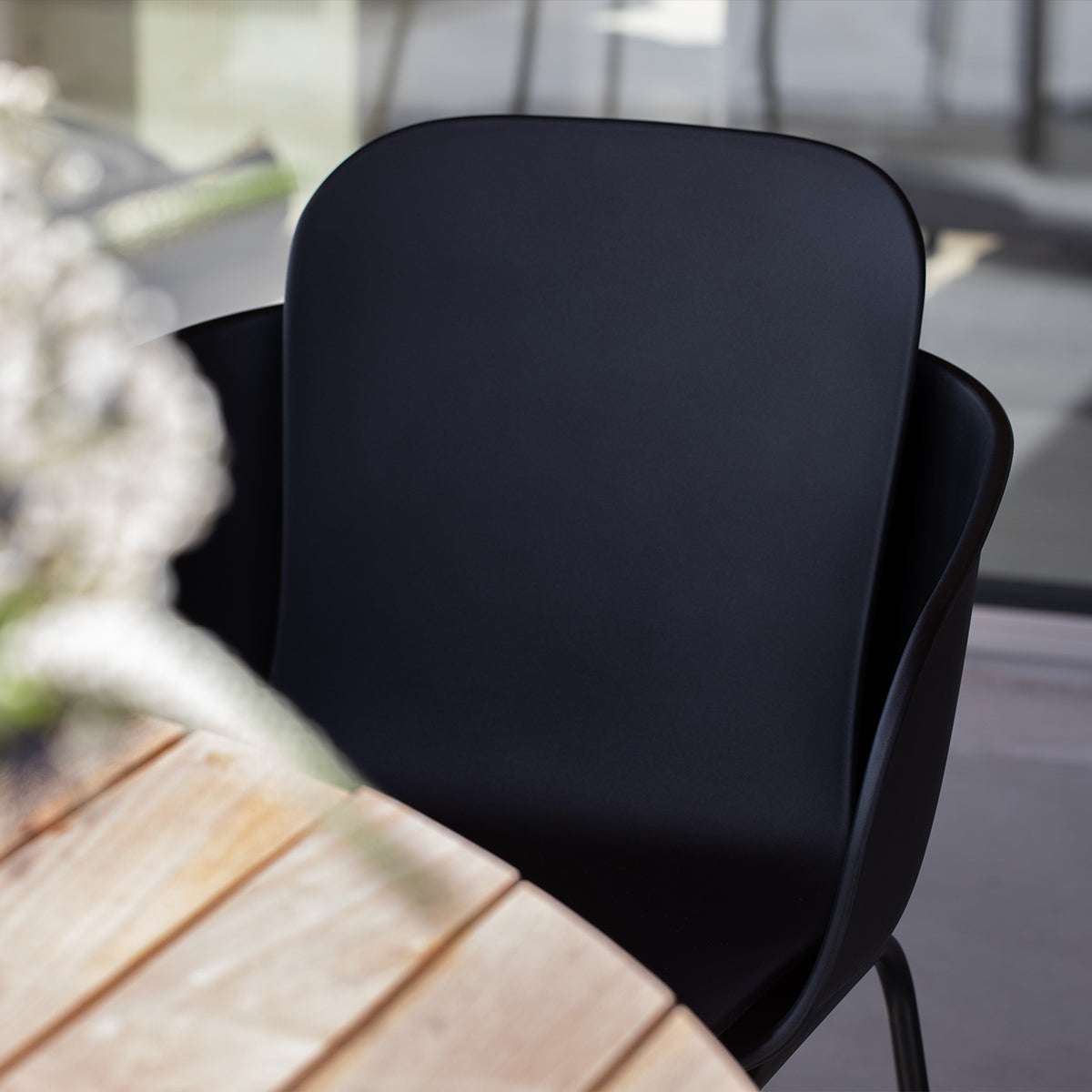 Zwarte outdoor eetkamerstoel met omhullende rugleuning aan een houten tuintafel van sackit ontworpen voor nordisch weer