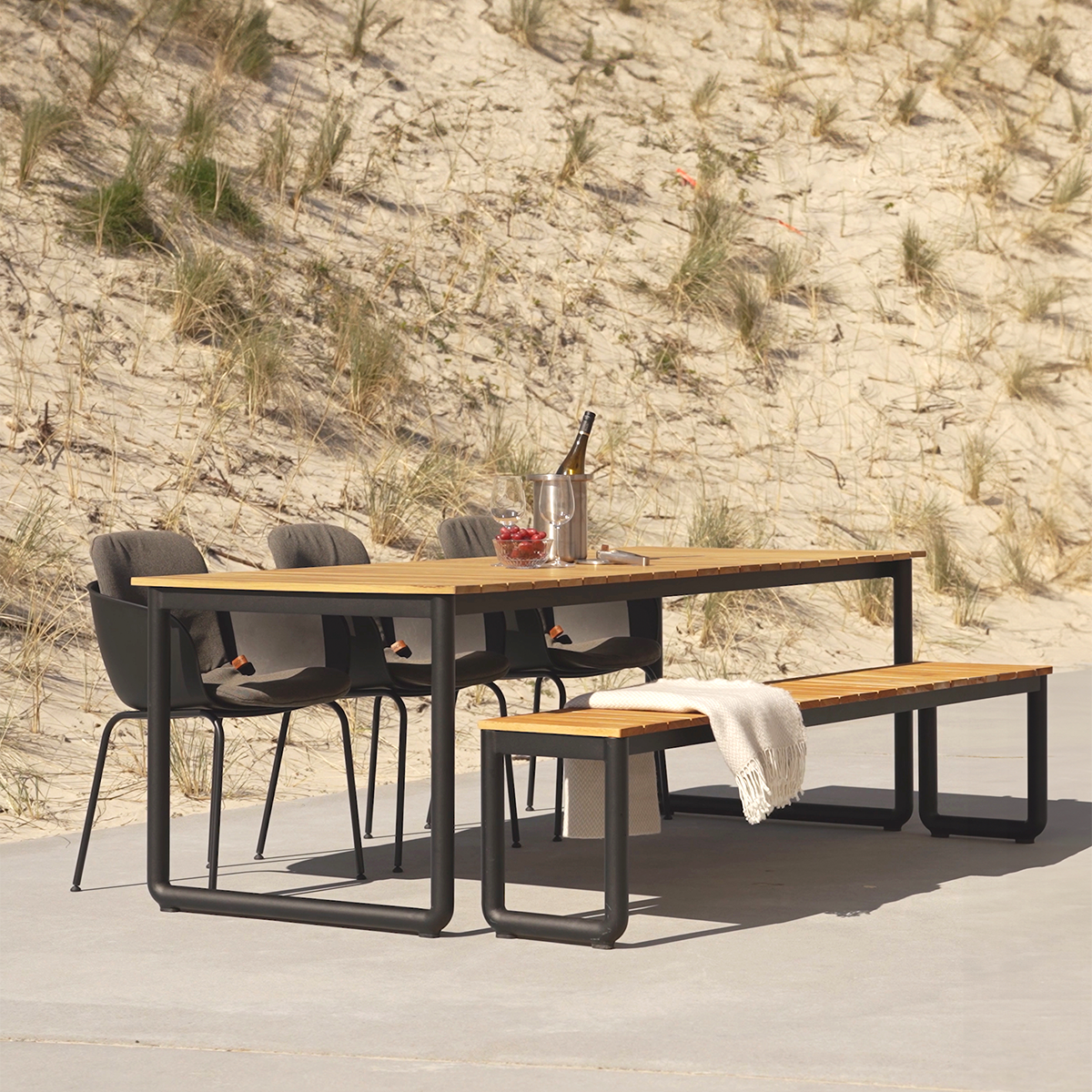 Buiten eetset met houten tafelblad en bankje met twee donkere stoelen in een duinlandschap van sackit voor stijlvol Scandinavisch buitenleven