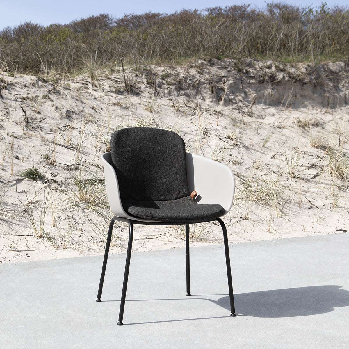 Zwarte en witte patio stoel van sackit met omarmende rugleuning op een zonnig terras bij de duinen geschikt voor buitengebruik en Scandinavisch design