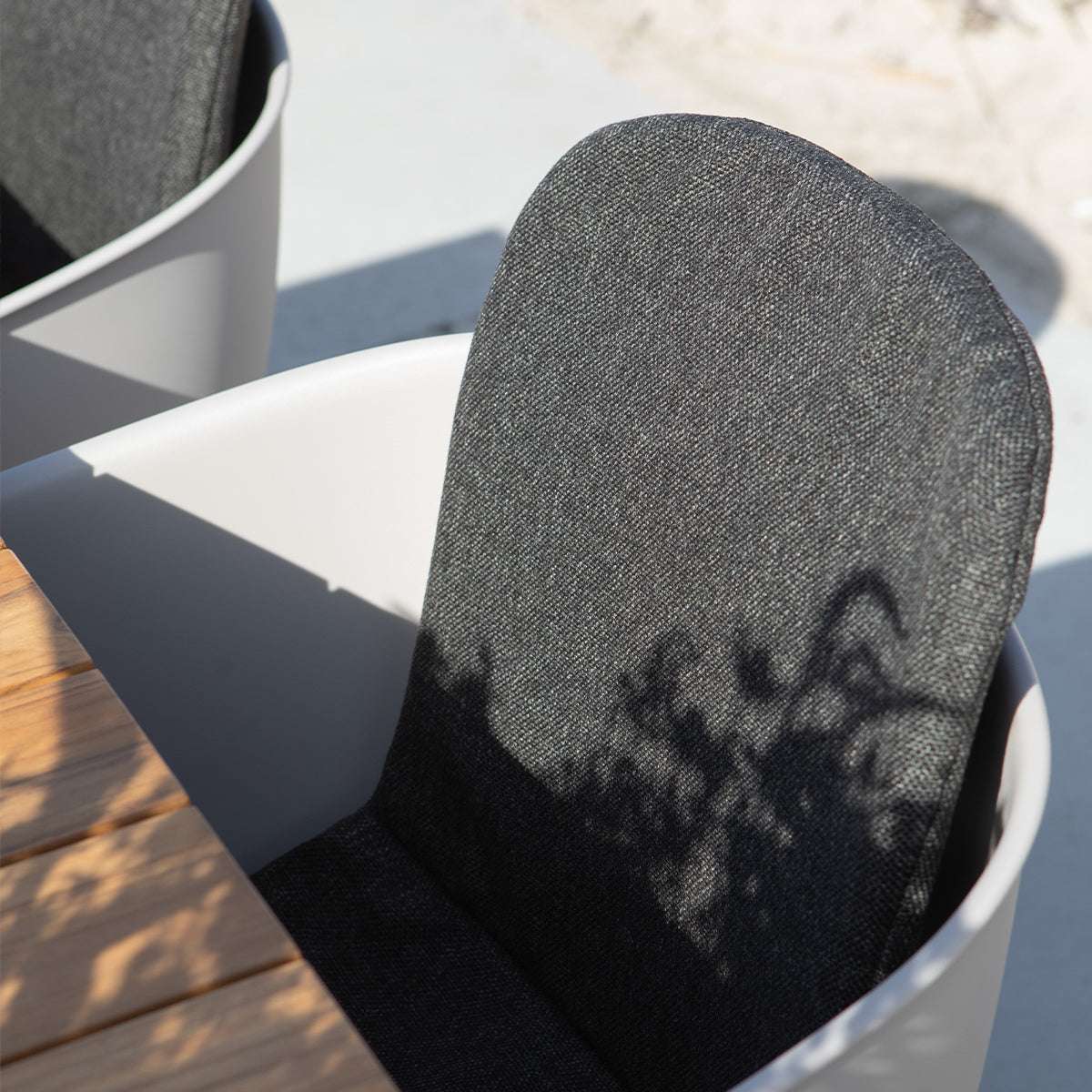 Donkergrijze tuinstoel met witte schaal en afgeronde rugleuning in zonlicht naast een houten buitentafel voor comfortabel buiten eten