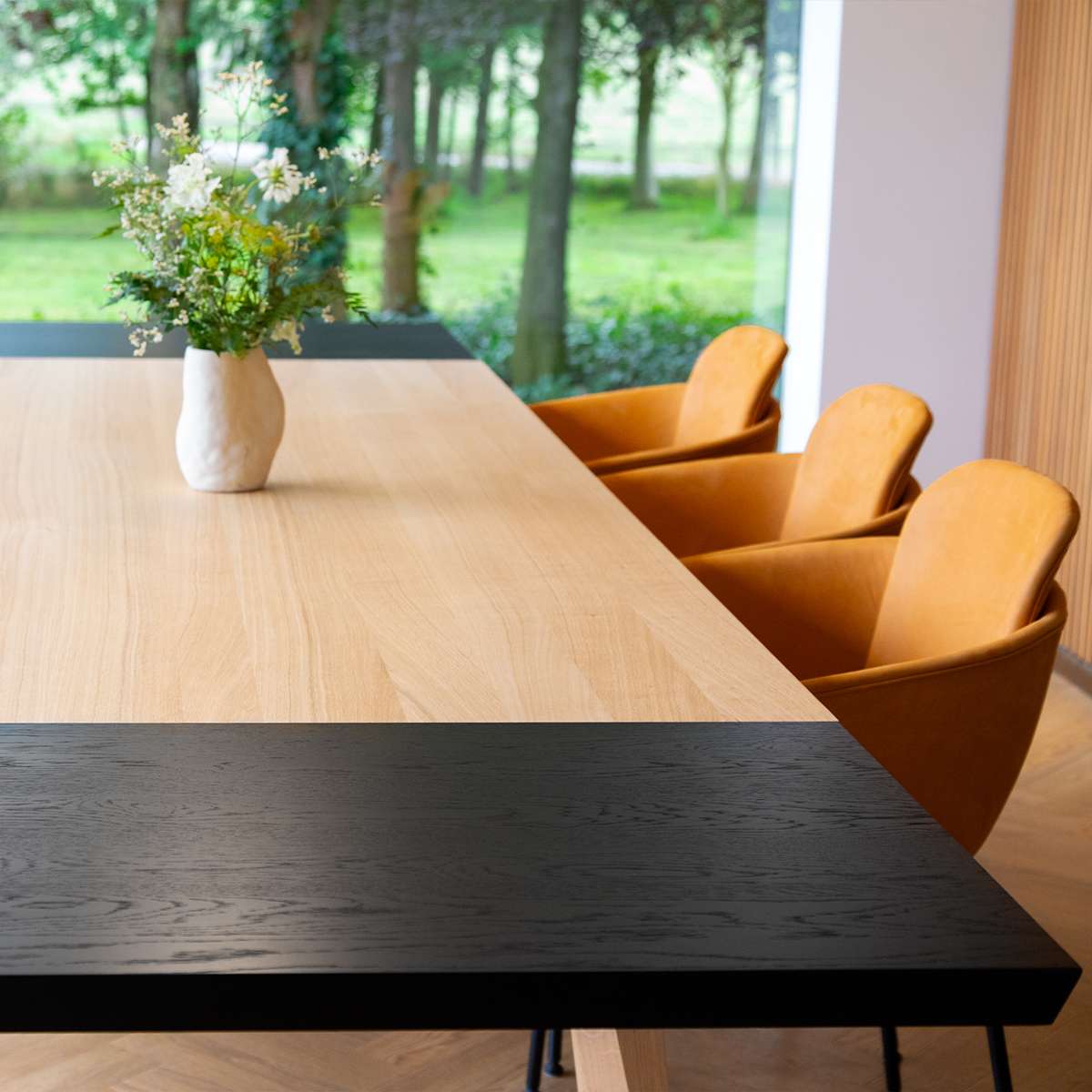 sackit eettafel met licht houten tafelblad en zwart eiken verlengblad met drie oranje stoelen en een vaas in een lichte eetkamer met uitzicht op de tuin