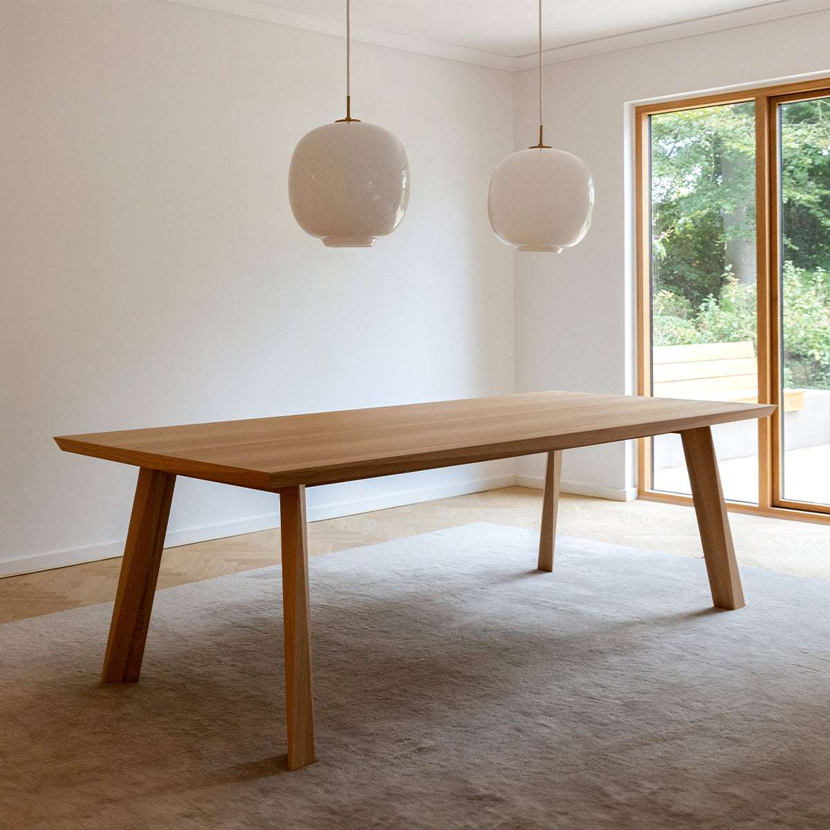 Lange eettafel van Europees eikenhout met gefacetteerd tafelblad en schuine poten in een lichte eetkamer van sackit ingericht in Scandinavische stijl
